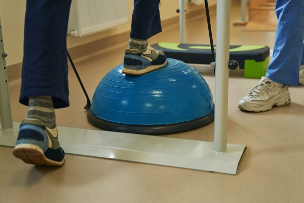 Cropped view on legs of stroke patient exercising on balance training platform during rehabilitation in clinic