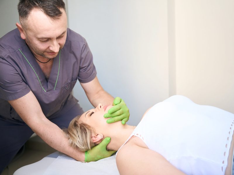 Osteopath performing cervical region traction on female patient lying on table in supine position