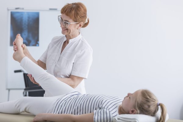 Happy female physiotherapist working with patient in pediatric scoliosis clinic